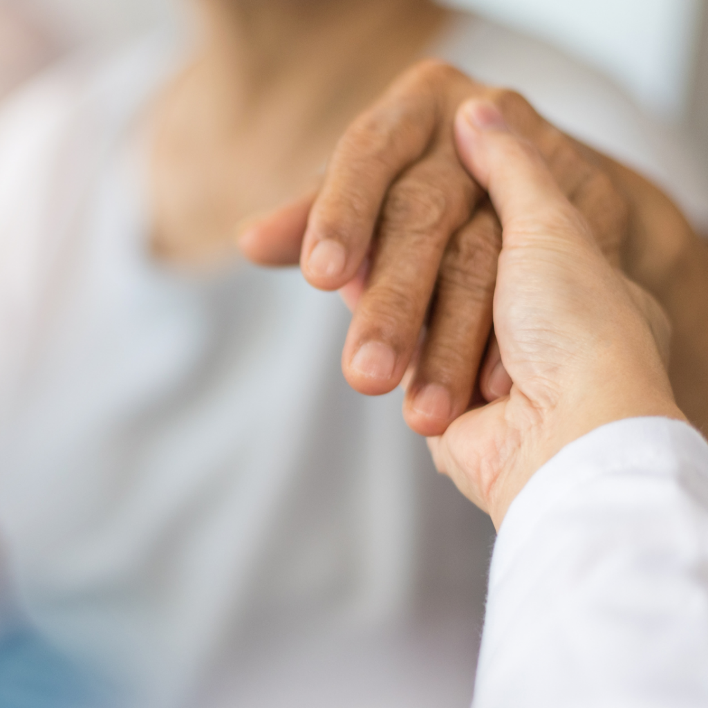 Gros plan sur la main d'un professionnel de santé en blouse blanche serrant la main d'une personne âgée