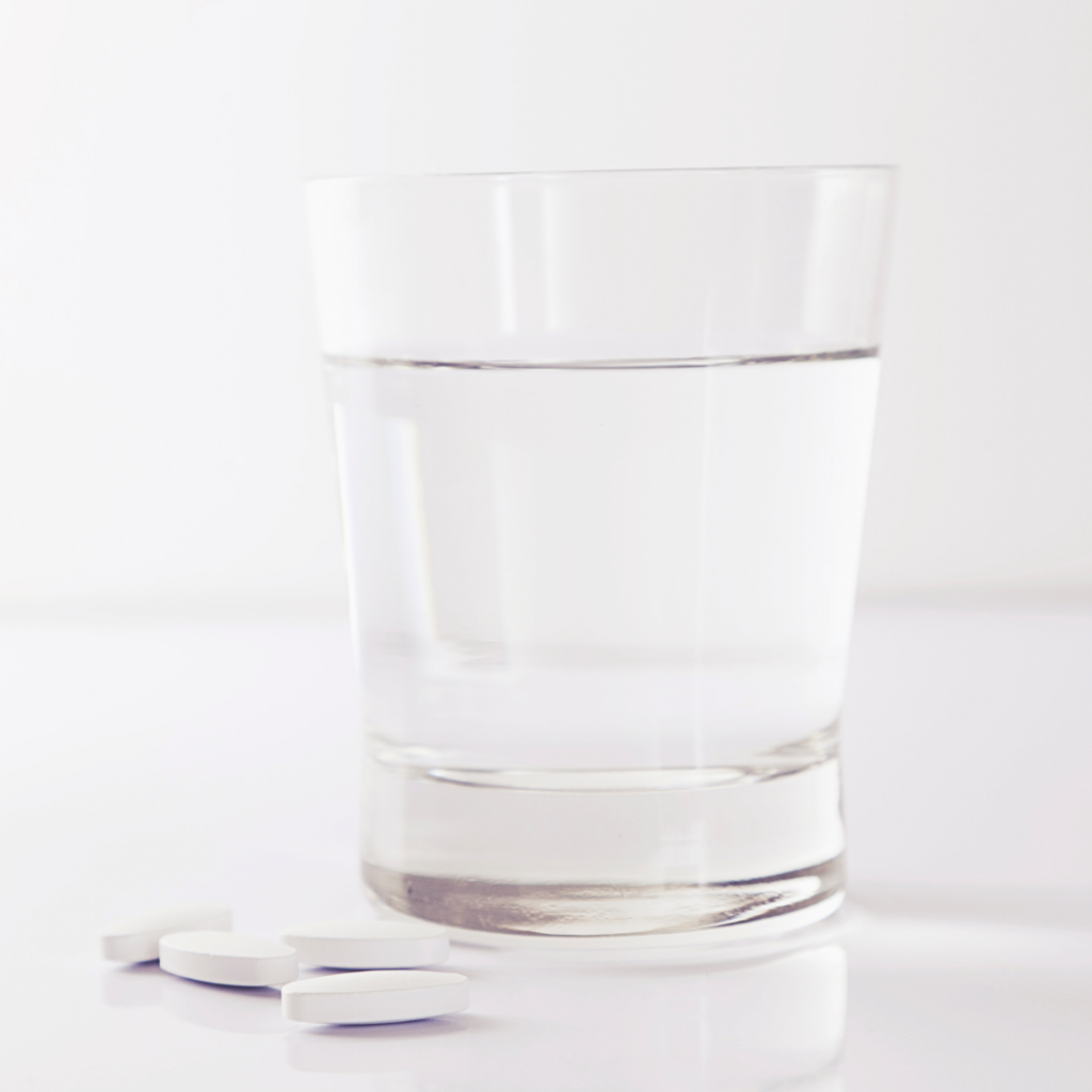 verre d'eau plein jouxtant des comprimés pour traiter une rhinite allergique avec des antihistaminiques