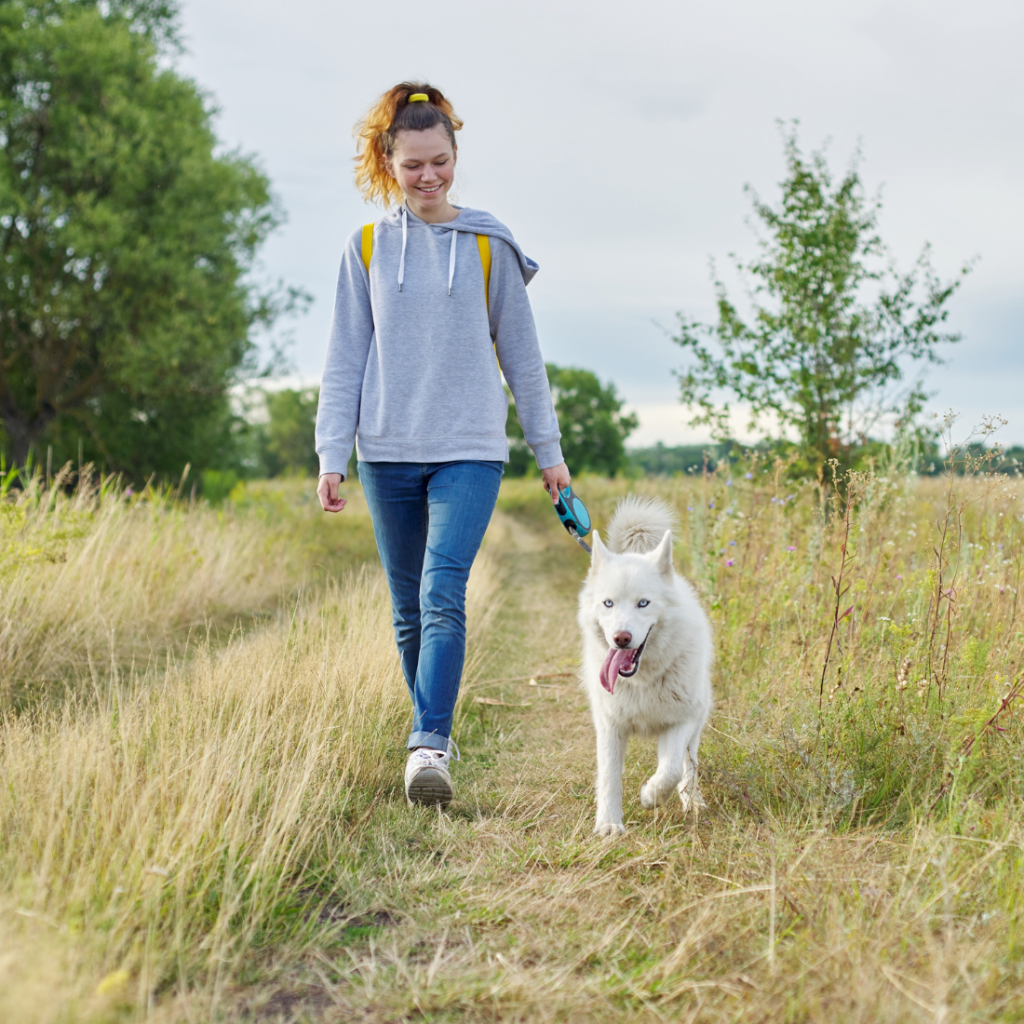 bienfait n°2 - jeune femme heureuse promenant son chien en pleine campagne 