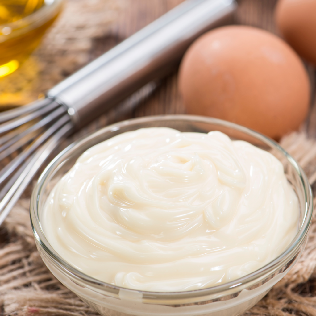 zoom sur une mayonnaise et ses ingrédients : huile, oeufs, et un fouet