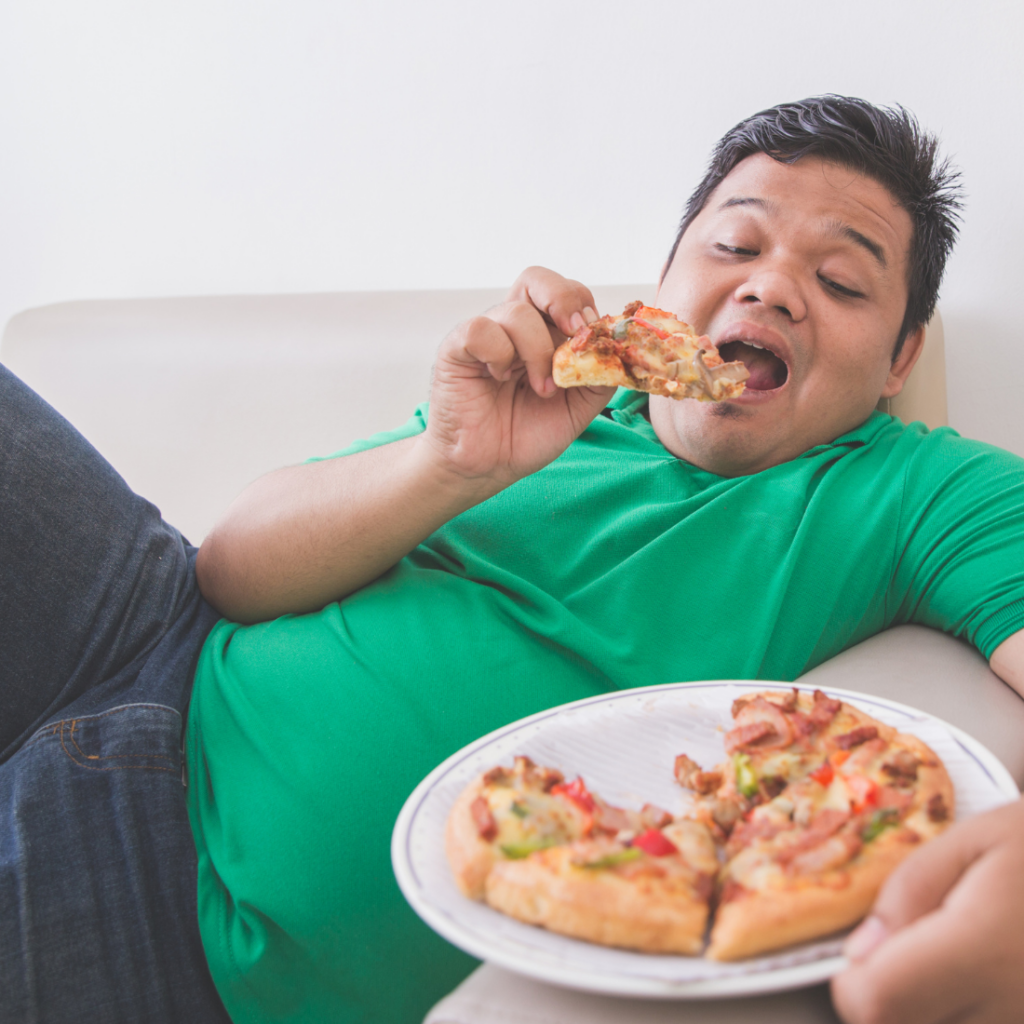 Adolescent en surpoids grignotant une part de pizza confortablement installé dans son canapé