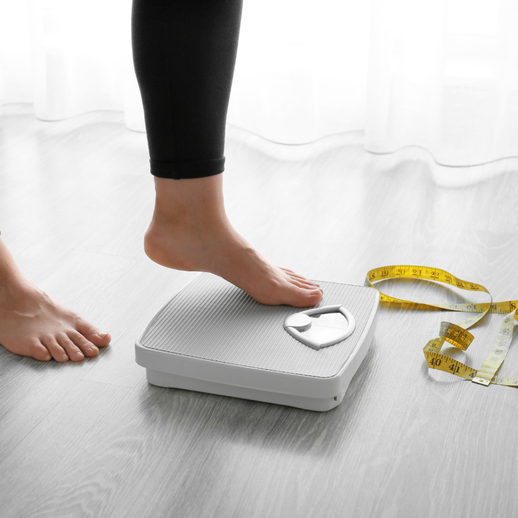 Pied d'une femme montant sur une balance blanche pour déterminer son imc et vérifier qu'elle n'est ni en surpoids ni obèse