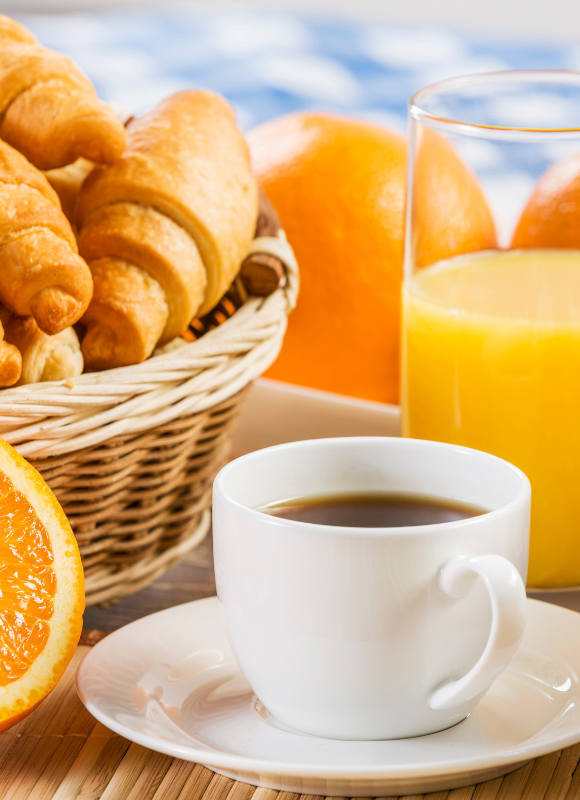 petit déjeuner énergétqiue comprenant une atsse de café, un verre de jus d'orange et des viennoiseries