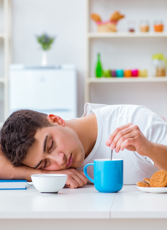 jeune homme dormant sur sa table et tournant sa tasse de café lors de la prise de son petit déjeuner