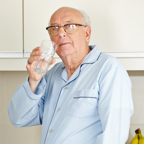 Homme âgé se servatn un verre d'eau dans sa cuisine