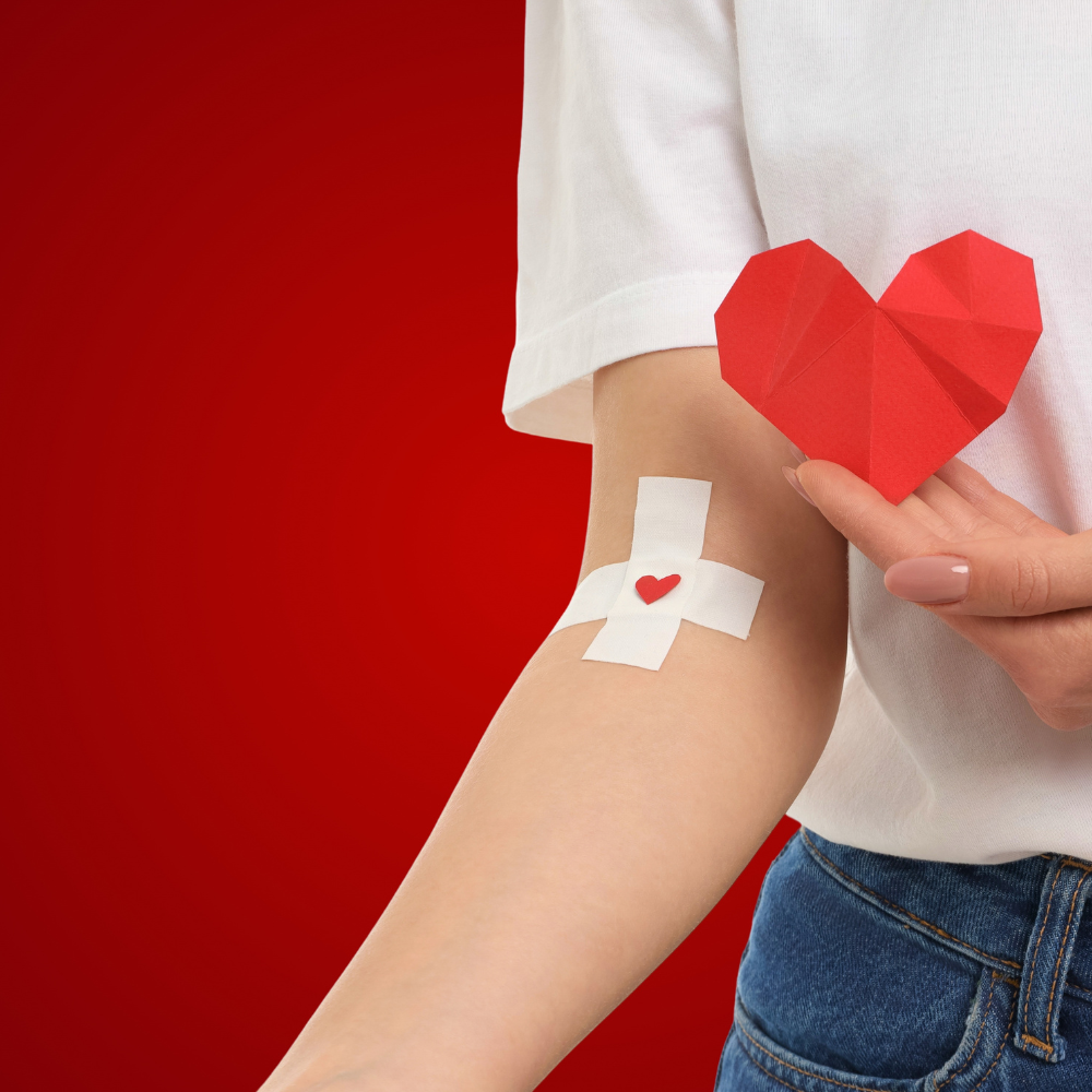 Gros plan sur un bras après un don de sang avec un pansement blanc orné d'un petit cœur rouge, symbole de solidarité.