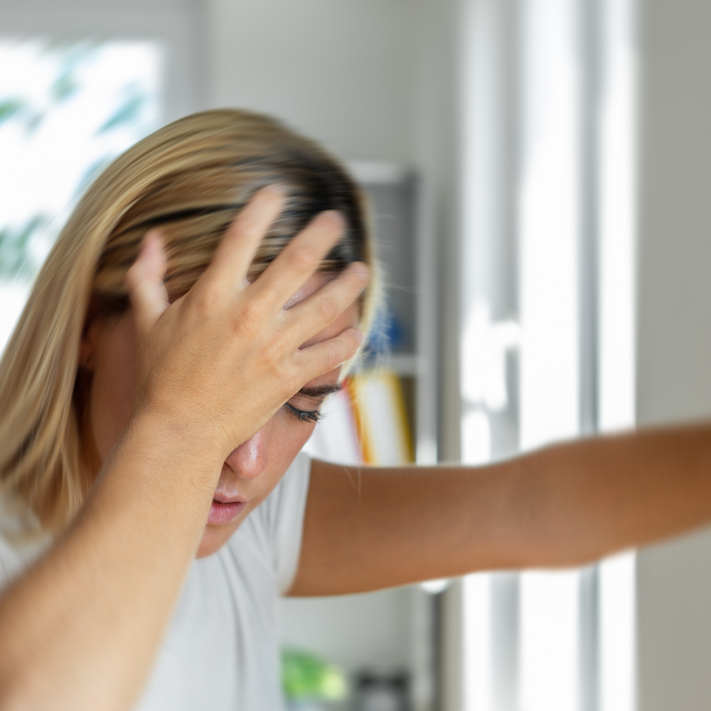 Une femme blonde de profil, la main sur le front, exprimant un vertige ou une confusion lors d'un trouble neurologique.