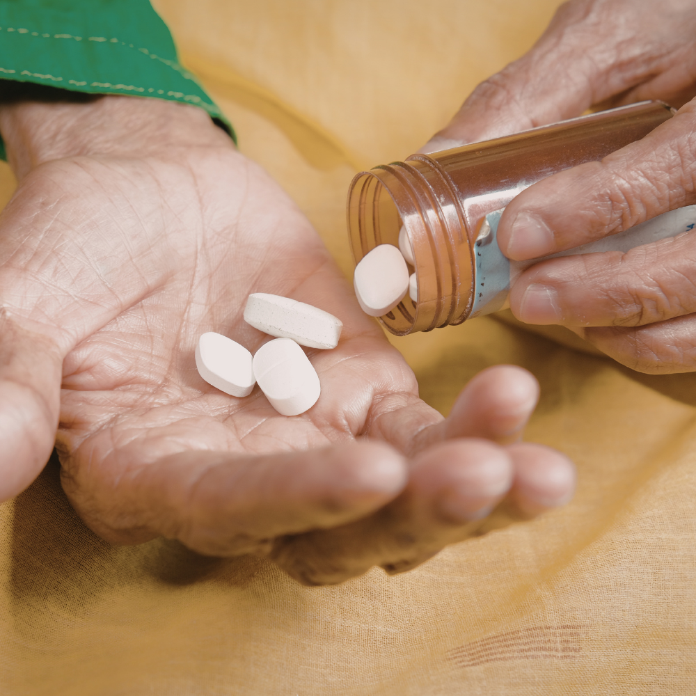 Gros plan sur les mains d'une personne âgée versant des comprimés blancs depuis un flacon dans sa paume pour son traitement anti-épileptique.